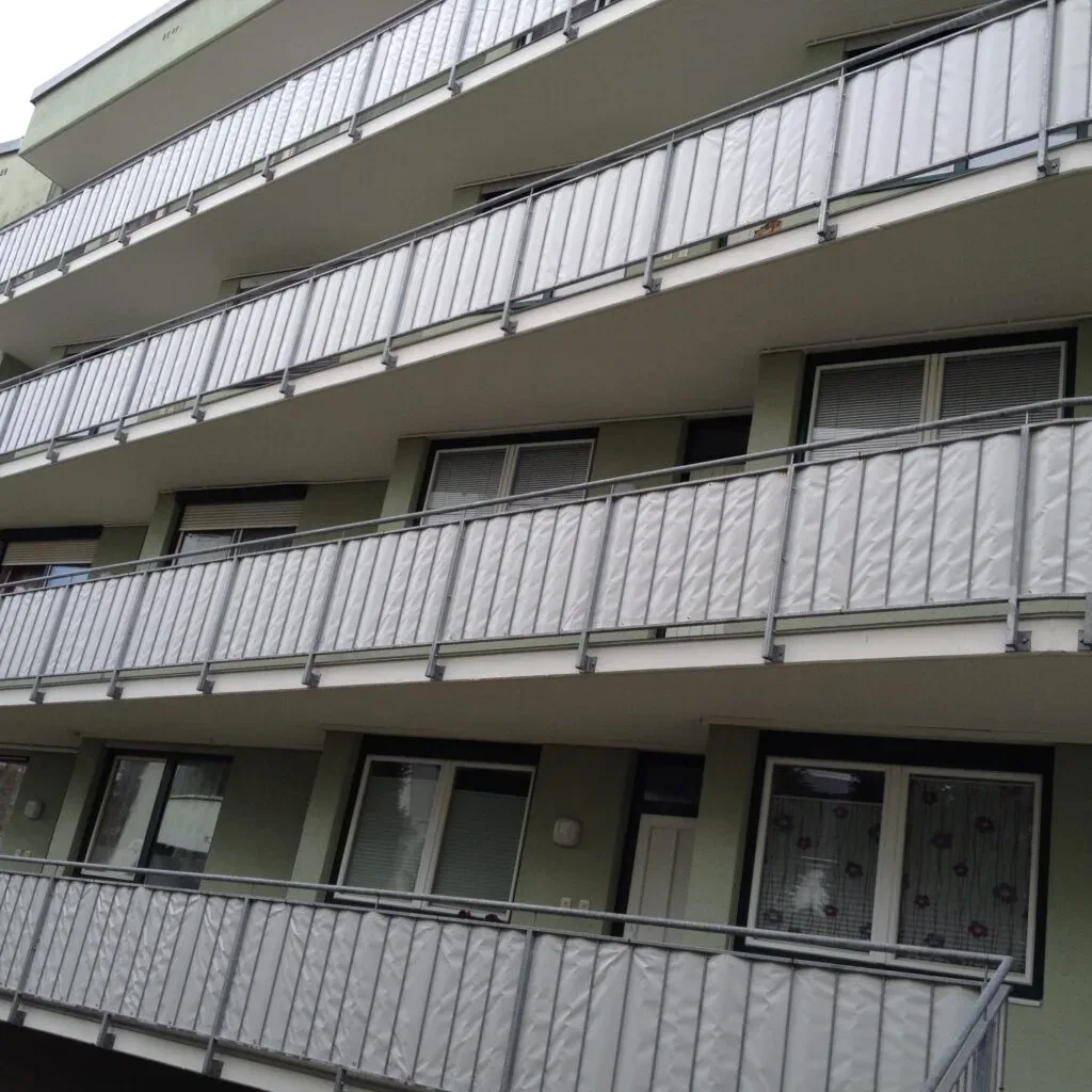 Mehrstöckiges Gebäude mit Balkonen, umgeben von grauen Trennwänden.