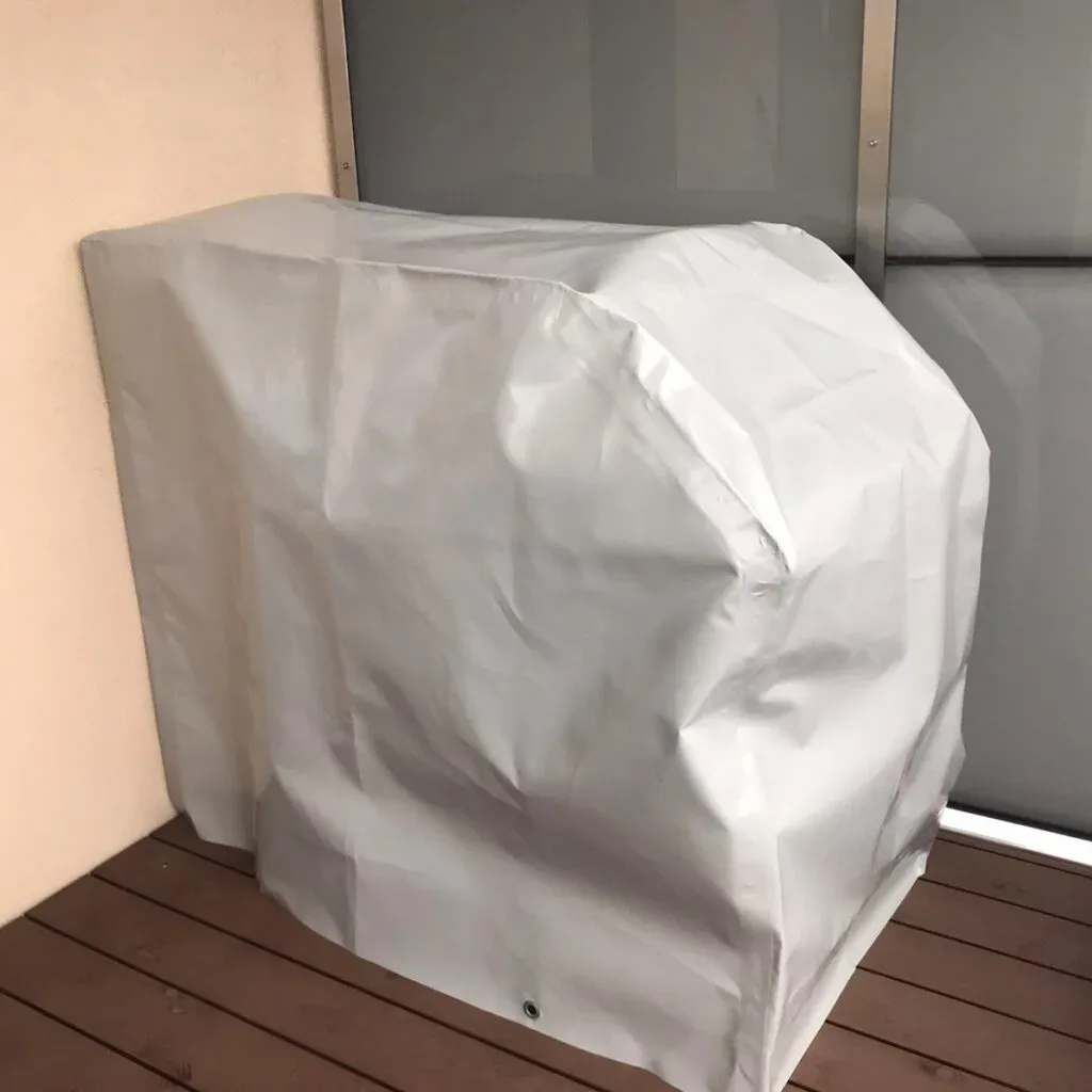 Abdeckplane schützt rechteckigen Gegenstand auf Holzboden vor dunkler Glastür.