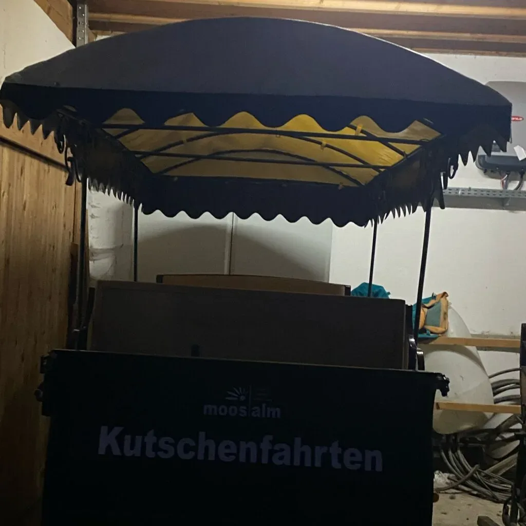 Planenbedeckter Kutschenanhänger mit Schriftzug "Kutschenfahrten" in einer Garage.