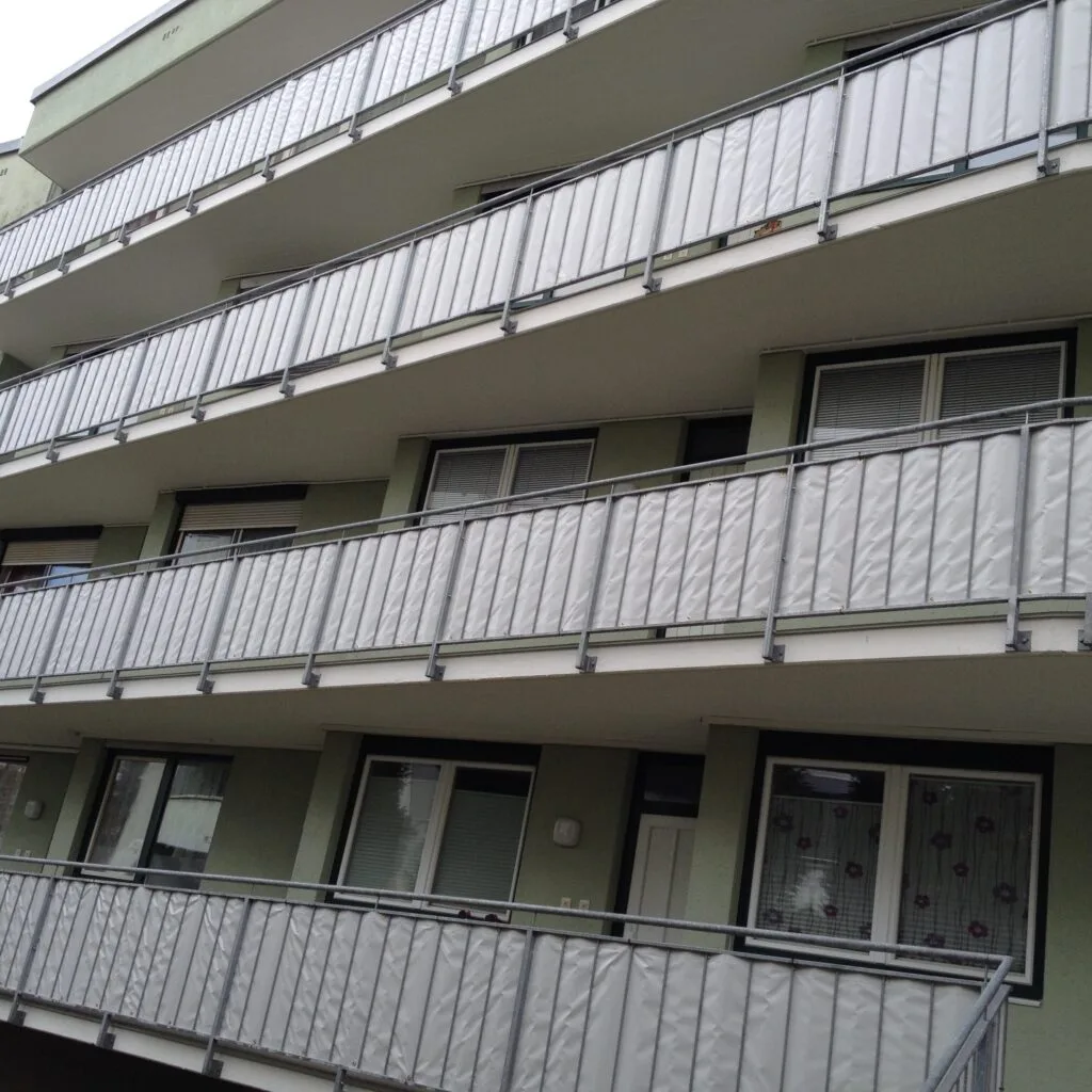 Mehrstöckiges Gebäude mit Balkonen, umgeben von grauen Trennwänden.